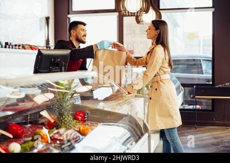 Verkäuferin, die Einkaufstasche an weibliche Kundin im Lebensmittelgeschäft abgibt Stockfoto