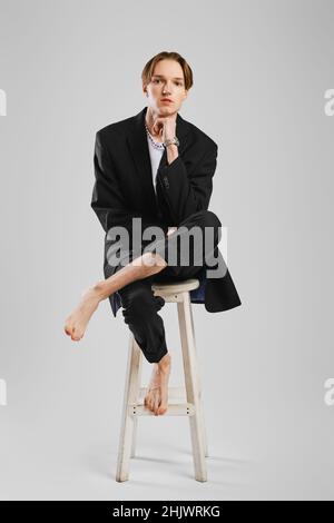 Ein junger Barfußmann in schwarzem Anzug sitzt auf einem hohen Stuhl im Studio Stockfoto