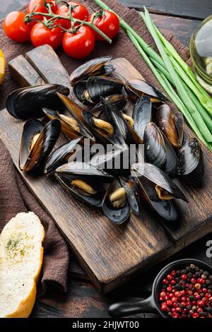 Gekochte Muscheln in Muscheln mit Gewürzen und Kräutern, auf Holzschneidebrett, auf altem dunklen Holztischhintergrund Stockfoto