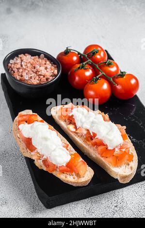 Ciabatta-Toasts mit Stracciatella-Käse, gehackten Tomaten und Basilikum. Weißer Hintergrund. Draufsicht Stockfoto