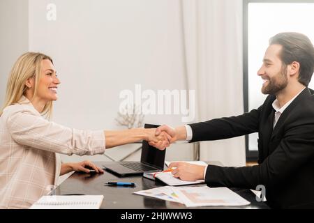 Attraktive junge Geschäftsfrau machte einen Deal mit ihrer Kollegin. Der Mann und die Frau schütteln die Hände und lächeln. Stock Foto Stockfoto