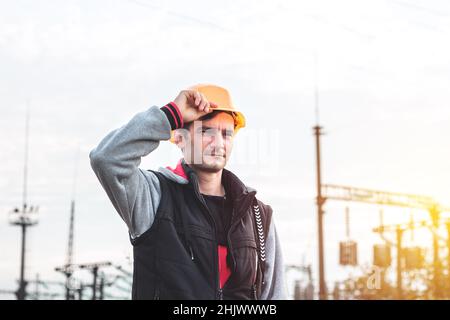 Arbeiter in einem Helm vor dem Hintergrund eines Umspannwerks und Hochspannungsmasten Stockfoto
