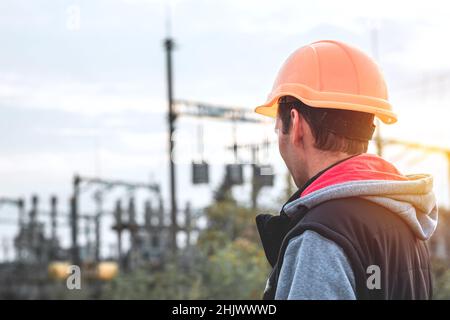 Arbeiter in einem Helm vor dem Hintergrund eines Umspannwerks und Hochspannungsmasten Stockfoto