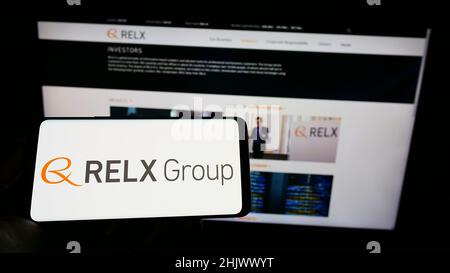 Person, die Mobiltelefon mit dem Logo des britischen Analyseunternehmens RELX Group plc auf dem Bildschirm vor der Business-Webseite hält. Konzentrieren Sie sich auf die Telefonanzeige. Stockfoto