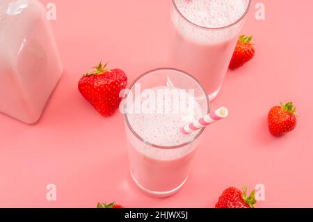 Erfrischende Desserts im Sommer und ein Konzept für kalziumreiche gesunde Getränke mit Gläsern Erdbeermilch, Glasflasche, gestreiften Trinkhalmen und verstreuten Strängen Stockfoto