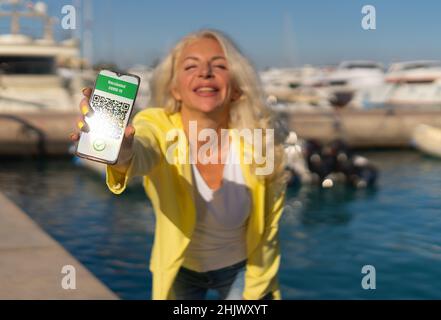 Frauen zeigen am Telefon einen Gesundheitspass mit einem Covid-Zertifikat Stockfoto