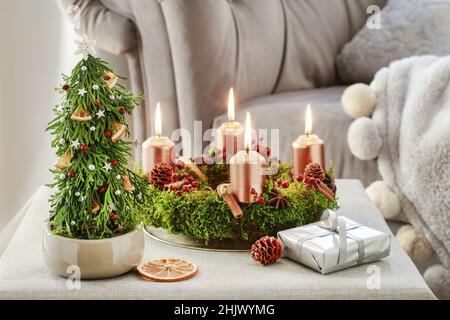 Weihnachtsbaum aus Thuja-Zweigen und Adventskranz aus Moos, Zimtstangen und rosa-Canina-Zweigen. Festliche Einrichtung Stockfoto