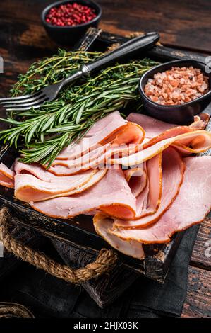 Italienische Prosciutto Cotto Schinken Scheiben in Holzschale mit Thymian und Rosmarin. Holzhintergrund. Draufsicht Stockfoto
