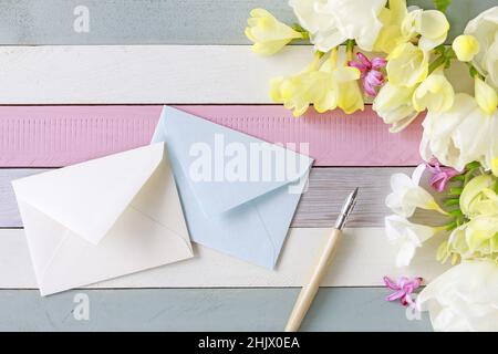 Schöne Freesias und Tulpen auf gestreiftem Holzhintergrund. Umschläge und Vintage-Stift zwischen Frühlingsblumen. Stockfoto