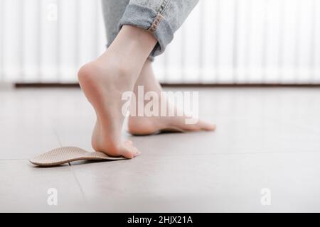 Frau, die orthopädische Innensohle innen anpasst, Nahaufnahme. Mädchen, das zu Hause eine Innensohle neben dem Fuß hält. Orthopädische Einlagen. Banner zur Fußpflege. Flache Füße Stockfoto