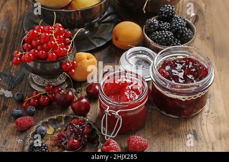 Gläser Kirschkerne Erdbeermarmelade zwischen Sommer und Herbst Früchte auf einem Holztisch. Stockfoto