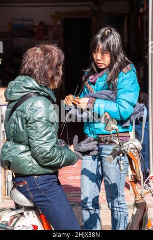 Zwei junge Frauen, die auf einer Straße in Jiashan, China, sprechen, eine strickt, die andere sitzt auf ihrem Motorrad. Stockfoto