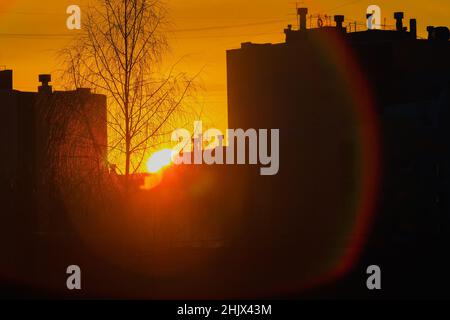 Sonnenuntergang in der Stadt zwischen mehrstöckigen Gebäuden. Silhouette von Häusern vor dem Hintergrund des Sonnenuntergangs. Atmosphärischer Hintergrund. Urbanisierung. Stockfoto