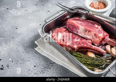 Rohe Tomahawk Kalbssteaks in Stahlblech mit Kräutern. Grauer Hintergrund. Draufsicht. Speicherplatz kopieren Stockfoto