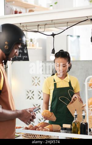 Mitarbeiter des Lebensmittelkarren, der eingewickelte Sandwiches in einen Papierbeutel legte, um ihm einen Kurier zu geben Stockfoto