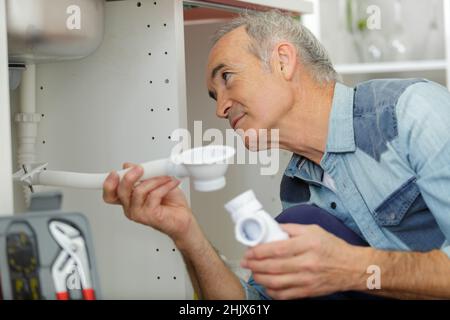 Senior Klempner Befestigung unter dem Waschbecken in der Küche Stockfoto