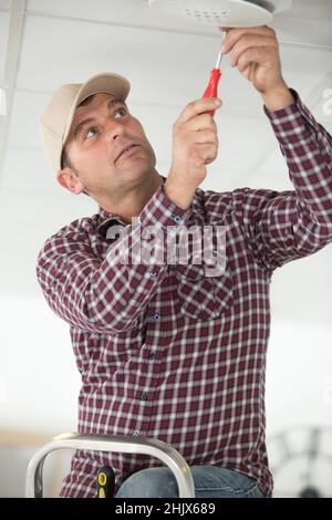 Arbeiter, der Rauchmelder an der Decke installiert Stockfoto