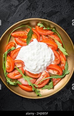 Italienische Salatkaprese mit Käse Stracciatella, Tomaten und Rucola. Schwarzer Hintergrund. Draufsicht Stockfoto