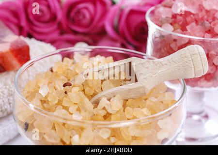 Glasschale mit gelbem Meersalz. Rosa Rosen im Hintergrund. Spa-Zeit Stockfoto