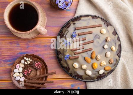 Hausgemachte Schokolade Brownie Kuchen mit Karamell-Creme und Mandeln mit Tasse Kaffee auf einem farbigen Holzhintergrund und Leinentextilien. Draufsicht. Flach legen Stockfoto
