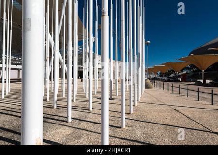 Gruppe von weißen Fahnenmasten, organisiert auf einem Platz im Parque das Nações / EXPO 98. Lissabon, Portugal. Gelbe Sonnenschirme auf der rechten Seite. Stockfoto