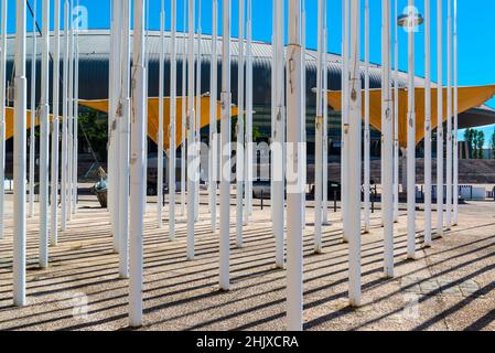 Gruppe von weißen Fahnenmasten, organisiert auf einem Platz im Parque das Nações / EXPO 98. Lissabon, Portugal. Gelbe Sonnenschirme und Altice Arena im Hintergrund. Stockfoto