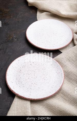 Zwei leere weiße Teller auf schwarzem Betongrund und Leinentextilien. Seitenansicht, Nahaufnahme. Stockfoto