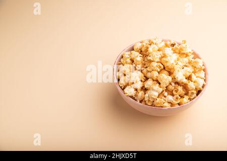 Popcorn mit Karamell in Keramikschale auf pastellorangefarbenem Hintergrund. Seitenansicht, Kopierbereich. Stockfoto