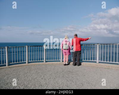 Touristen, die sich an einem Aussichtspunkt am Meer mit blauem Meereshimmel im Freien verkleidet haben - Kilt Rock & Mealt Falls Viewpoint, Isle of Skye, Schottland, Großbritannien Stockfoto