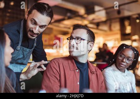 Der Kellner sprach mit Freunden im Restaurant während des Abendessens Stockfoto