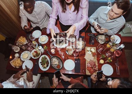 Frau fotografiert auf dem Smartphone, während sie mit Freunden im Restaurant zu Abend iß Stockfoto