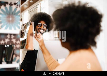 Lächelnder männlicher Friseur, der im Salon Kosmetikprodukte an weibliche Kunden verkauft Stockfoto