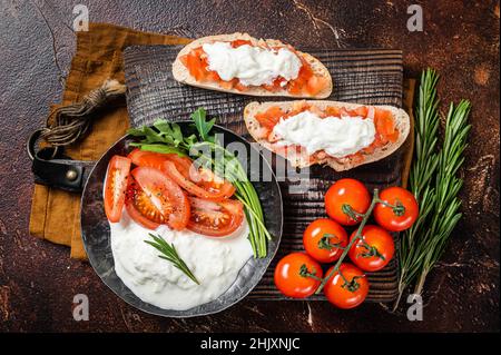 Bruschettas mit Stracciatella-Käse, gehackten Kirschtomaten und Rosmarin. Dunkler Hintergrund. Draufsicht Stockfoto