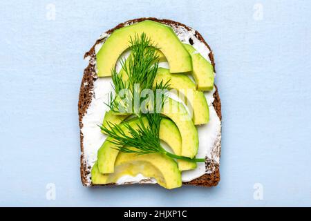Auswahl an Sandwiches zum Frühstück - Scheibe Vollkornbrot, Frischkäse, Avocado garniert mit grünem Dill auf blauem Tisch Draufsicht Flat Lay Stockfoto