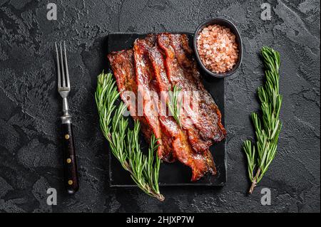 Gebratene, knusprige, streakige Bacon-Streifen. Schwarzer Hintergrund. Draufsicht Stockfoto