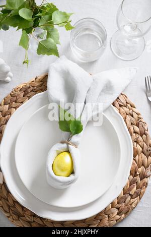 Ostern elegante Tischkulisse mit gelbem Ei, frischem Grün auf grauer Leinentischdecke. Blick von oben. Christliche Religionstradition. Stockfoto