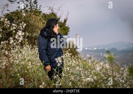 Junges Mädchen, das am Morgen auf dem Gipfel des Berges steht, mit weißen Blumen im Vordergrund Stockfoto