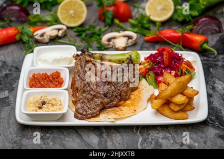 Gegrillte Lammkoteletts mit pommes Frites und Vorspeisen auf einem weißen Porzellanteller Stockfoto