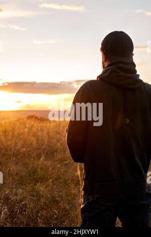 Blick von hinten auf nicht erkennbaren Mann, der den Sonnenuntergang betrachtet, in Kontemplation. Rückansicht. Junger Mann denkt, nach dem Sport-Training im Freien. Menschen am lebtesten Stockfoto