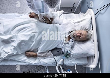 Draufsicht auf ältere kranke Männer injiziert, im modernen Klinikkrankenhaus, unter der Dropper, abgeschnitten Krankenschwester. Blick von oben. Medizin, Gesundheit, krank Stockfoto