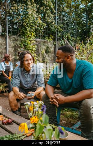 Lächelnde männliche und weibliche Freiwillige sprechen, während sie auf einer städtischen Farm sitzen Stockfoto