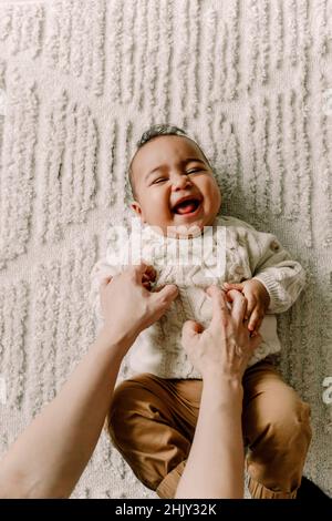 Zugeschnittenes Bild der Mutter, die einen kleinen Jungen kitzelt, der auf einer Decke liegt Stockfoto