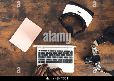 Schreibtisch aus dunklem Holz mit Laptop VR Headset alte Fotokamera und pinkes Notebook – über der Oberseite. Hochwertige Fotos Stockfoto