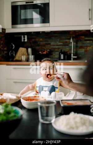 Zugeschnittenes Bild vom Vater, der einen Jungen am Esstisch in der Küche füttert Stockfoto