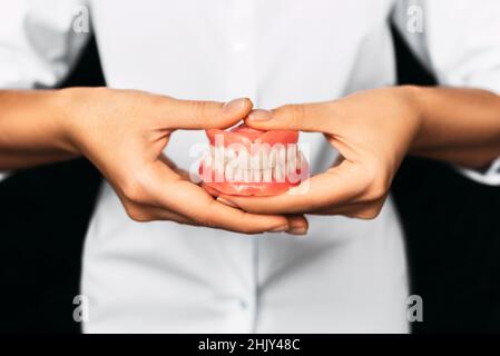 Der Zahnarzt hält Prothesen in den Händen. Zahnprothese in den Händen des Arztes Nahaufnahme. Vorderansicht der kompletten Prothese. Zahnmedizin Konzept Stockfoto