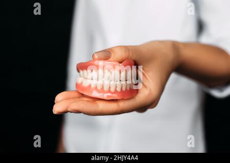 Der Zahnarzt hält Prothesen in den Händen. Zahnprothese in den Händen des Arztes Nahaufnahme. Vorderansicht der kompletten Prothese. Zahnmedizin Konzept Stockfoto