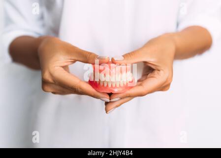 Der Zahnarzt hält Prothesen in den Händen. Zahnprothese in den Händen des Arztes Nahaufnahme. Vorderansicht der kompletten Prothese. Zahnmedizin Konzept Stockfoto