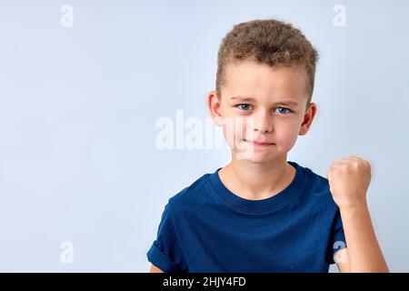 Hübscher Junge sieht wütend aus. Das Kind ist beleidigt, droht, zeigt eine Faust. Ärgerliches, verärgerliches, aggressives Kind. Porträt auf weißem Studiohintergrund. Chi Stockfoto