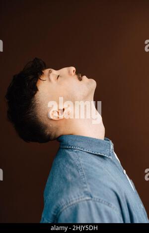 Seitenansicht des jungen Mannes auf braunem Hintergrund Stockfoto