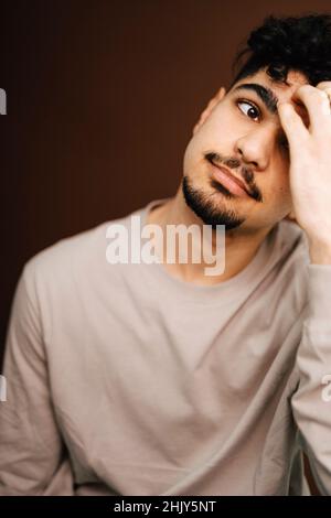 Müder Mann mit Kopf in der Hand vor braunem Hintergrund Stockfoto